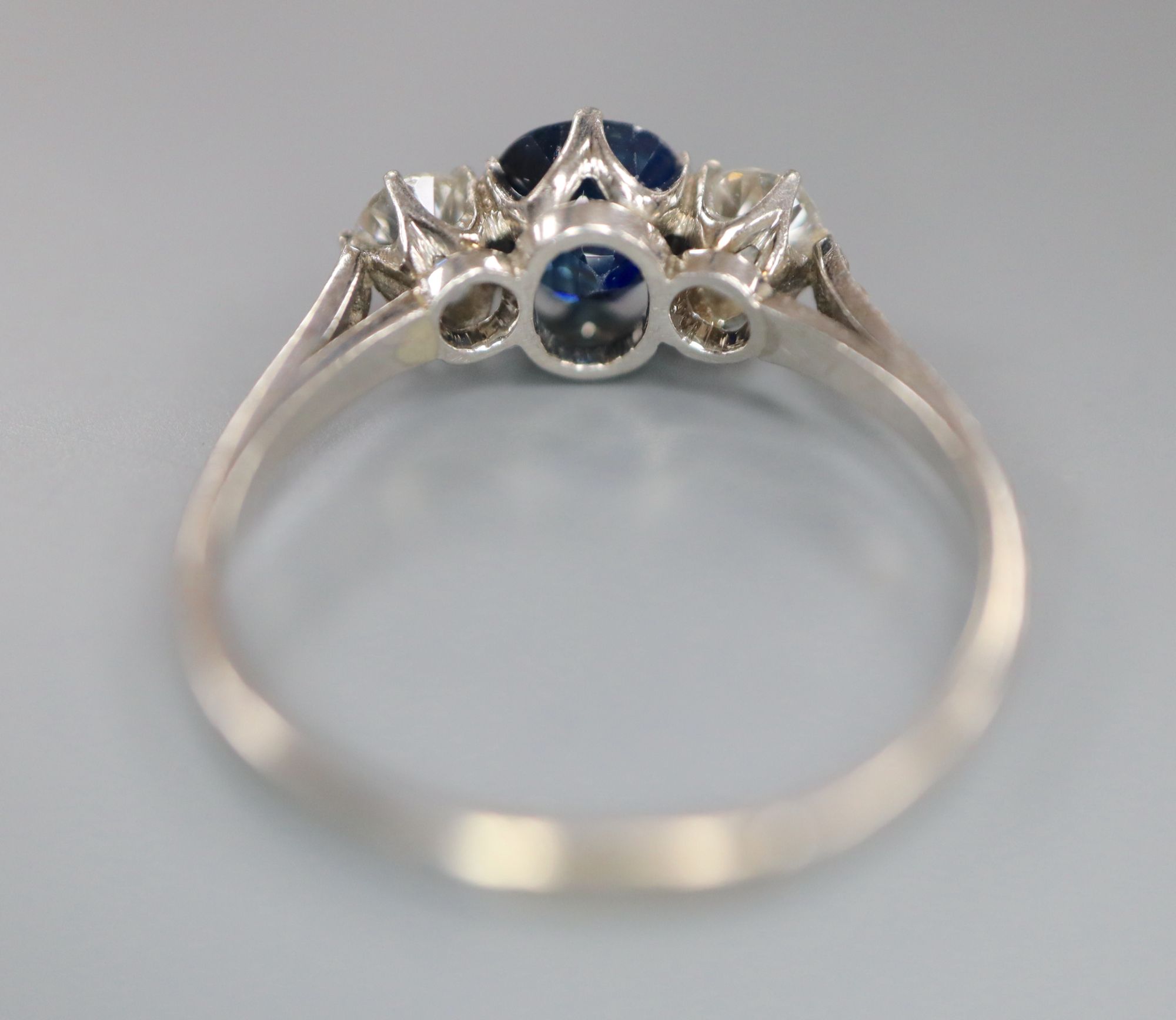 A white metal, sapphire and diamond three stone ring, with diamond chip set shoulders, size Q, gross 3.6 grams.